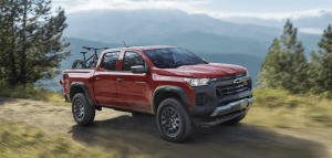 red Chevrolet Colorado driving on dirt road with trees and mountains in background